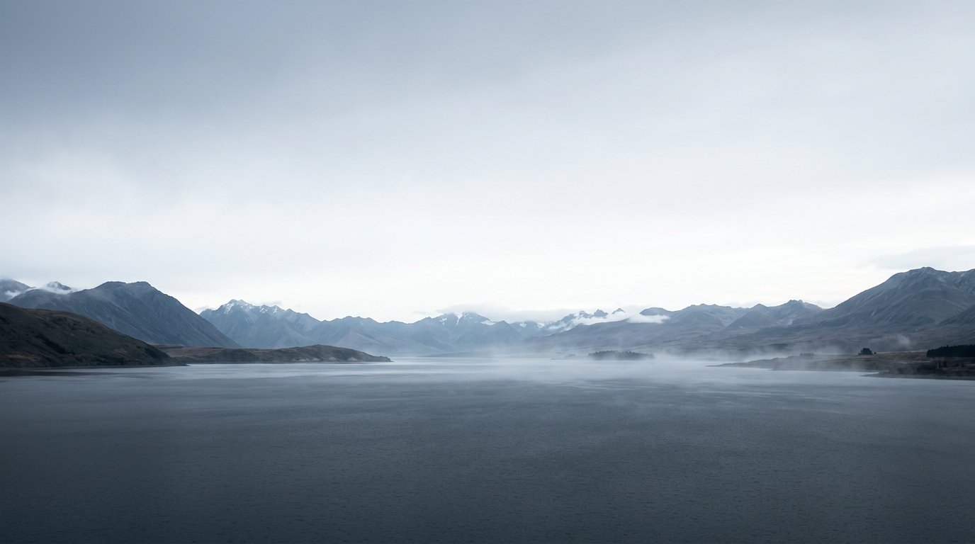 Serene view across a Southern Alps lake with distant mountain ranges and low mist