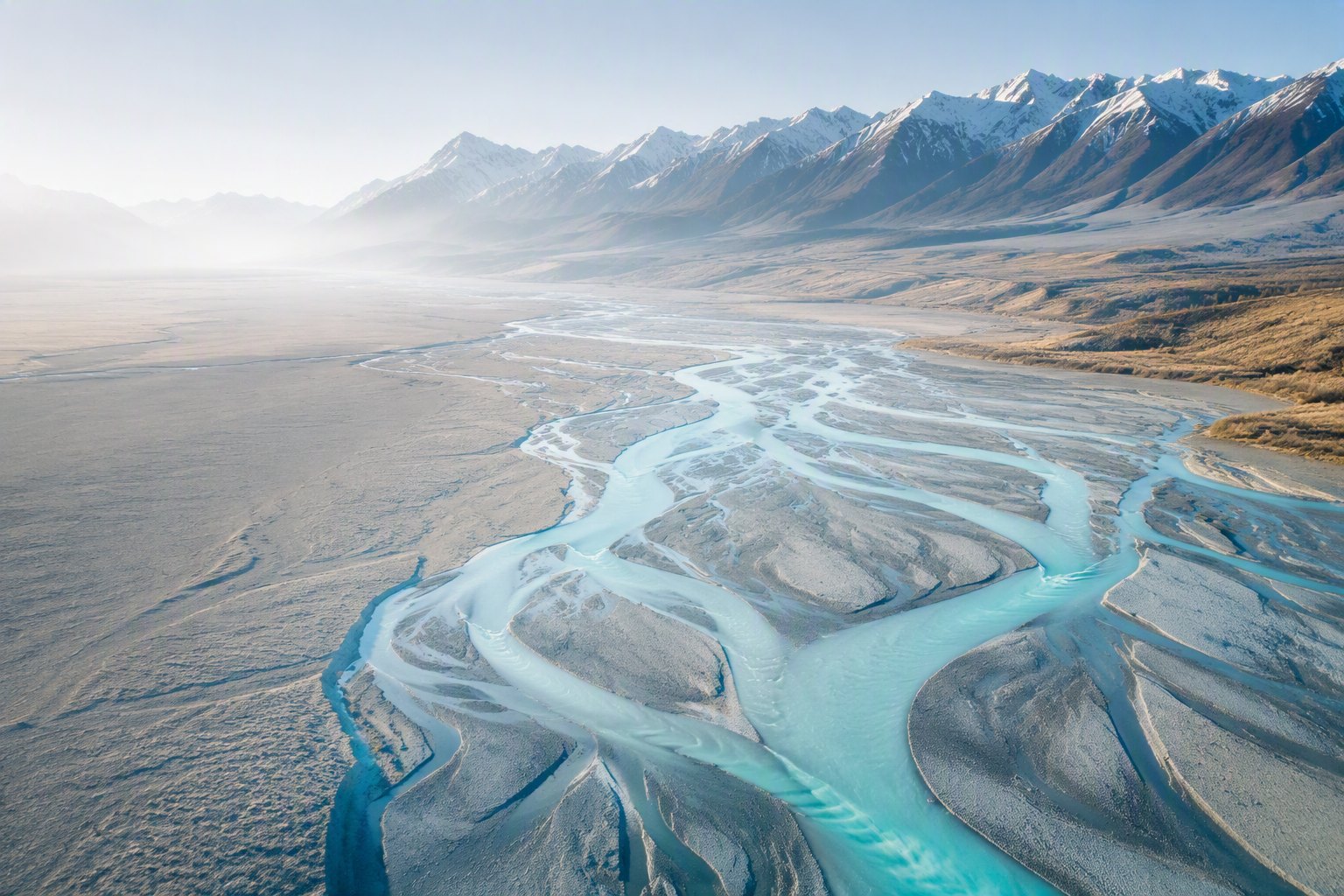 Aerial view of a New Zealand Canterbury braided river with turquoise channels branching across a pale valley below the snow-dusted Southern Alps